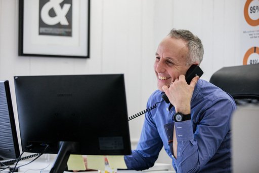 A man talking on the phone while smiling and looking at his computer screen
